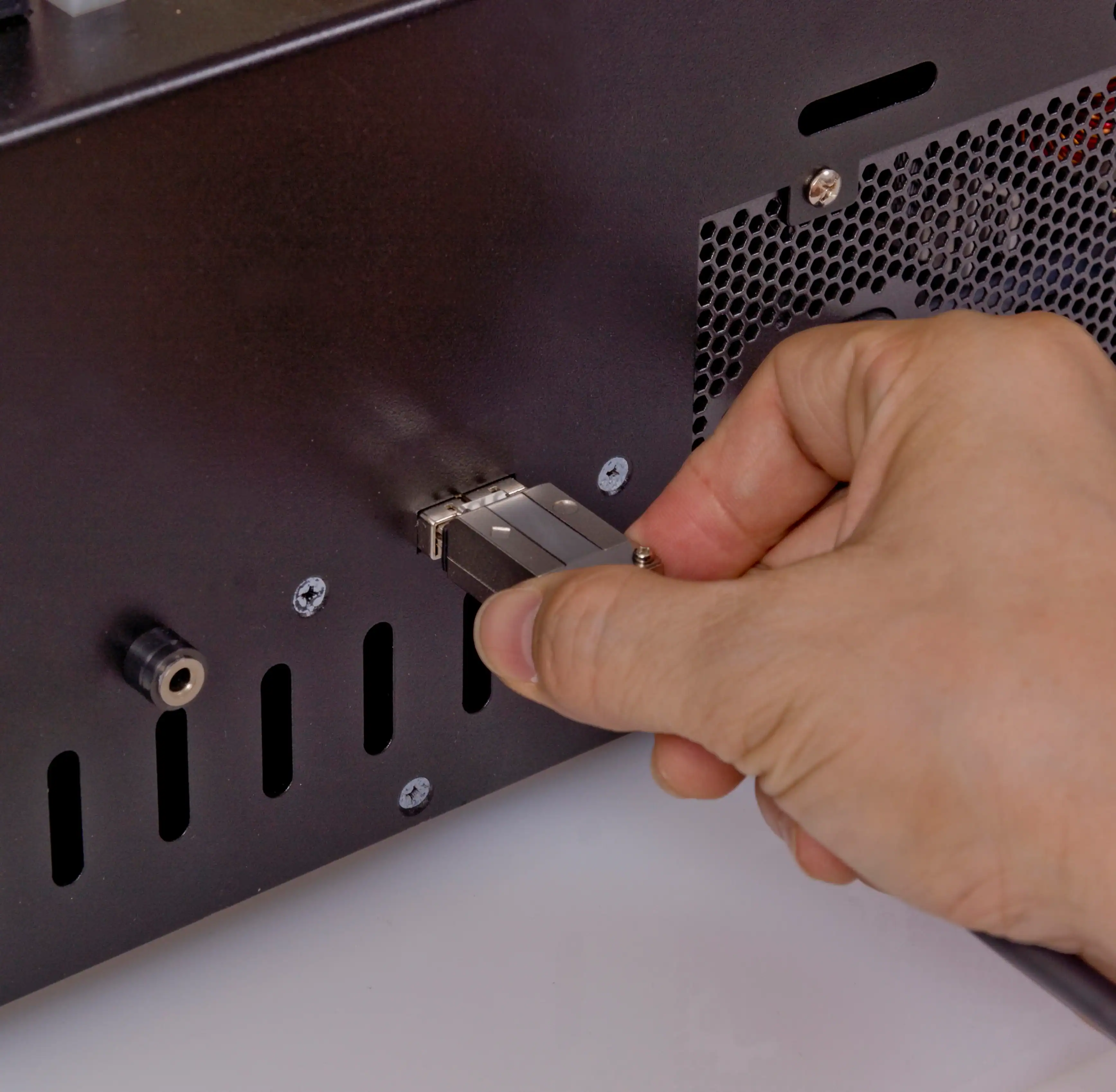 A hand plugs a large silver connector into the back panel of an MTC Series SATA/IDE HDD/SSD Daisy-Chain High Speed Duplicator and Sanitizer 1-15, which features ventilation holes and multiple ports for managing several drives.